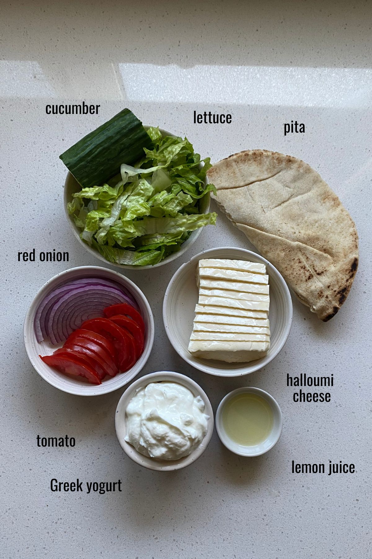 Ingredients for a halloumi pita in dishes on a white counter top with text.