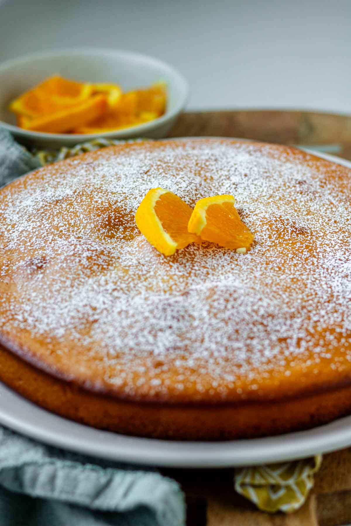 An orange blossom cake on a white plate topped with powdered sugar and orange slices.