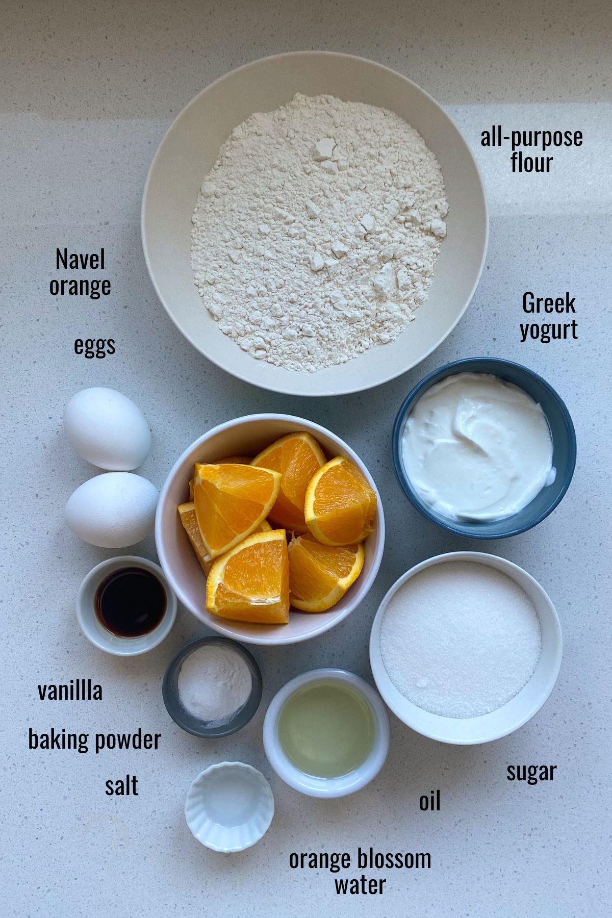 Ingredients for an orange blossom cake on a white counter top with black text indicating each ingredient.