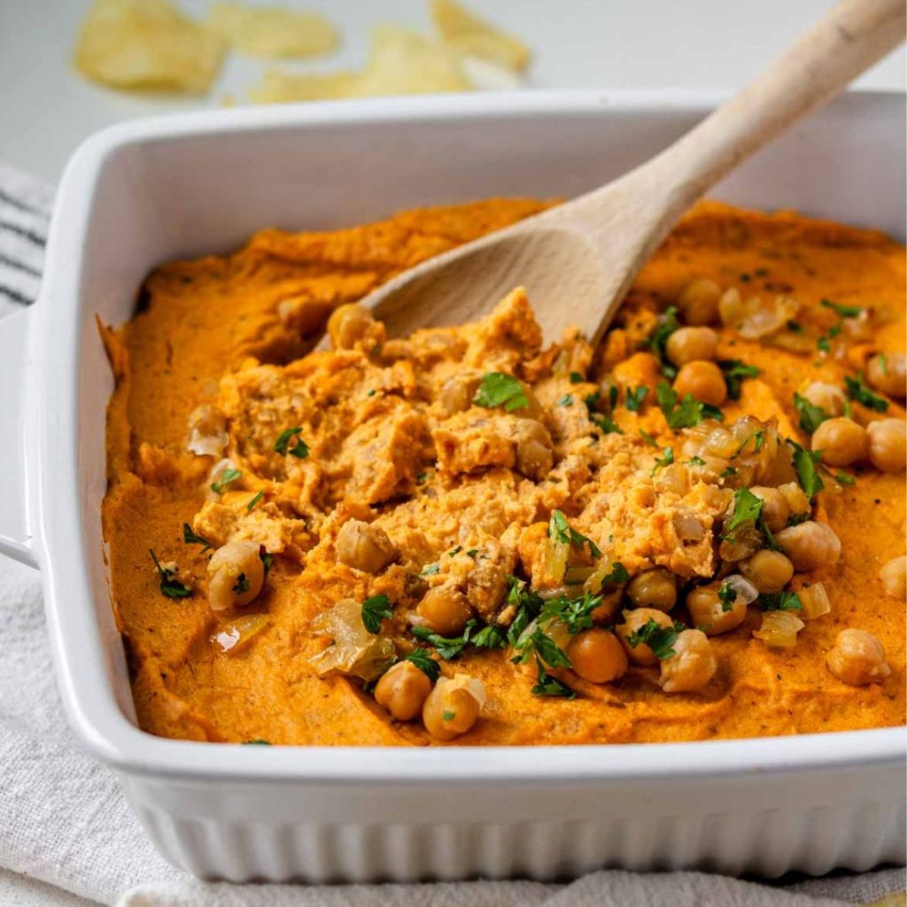 Vegan buffalo dip in a white baking dish topped with chickpeas and parsley.