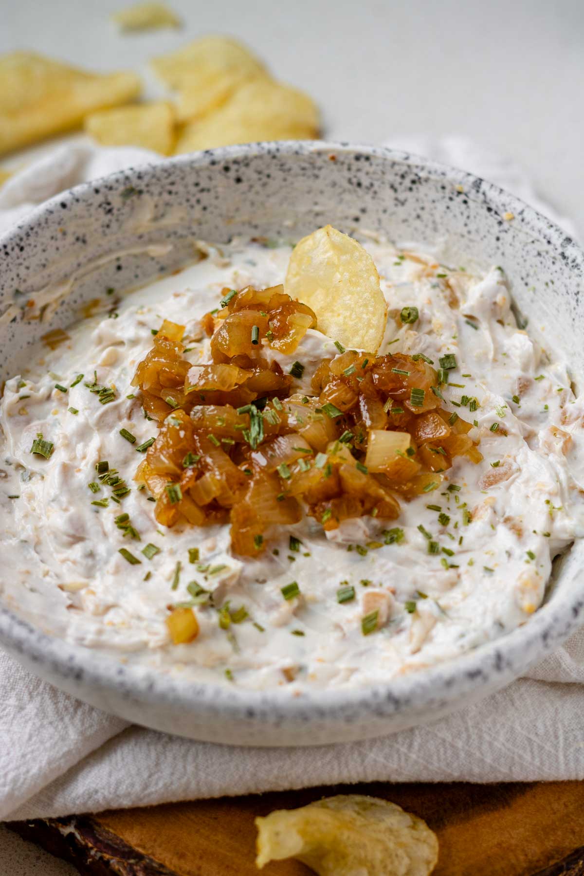 A white bowl of French onion dip topped with caramelized onions and a potato chip.