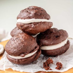 Vegan whoopie pies on a piece of parchment paper on a wooden platter.