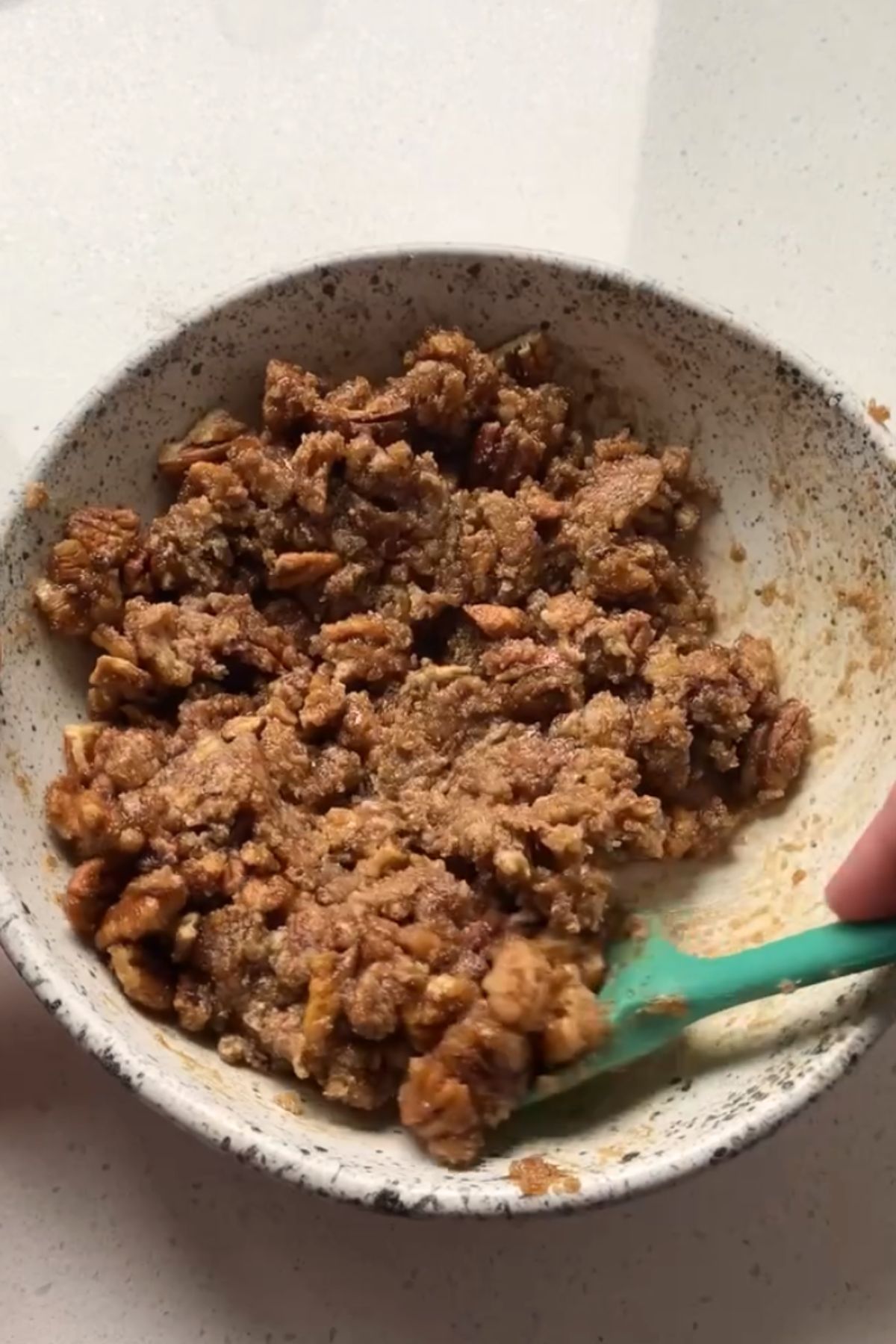 A maple pecan danish filling in a white speckled bowl with a green silicone spatula.