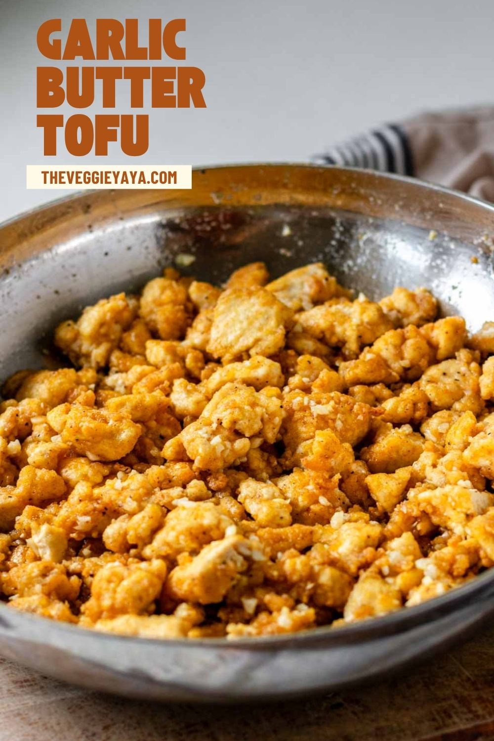 Garlic butter tofu in a stainless steel pan with dark orange text above.