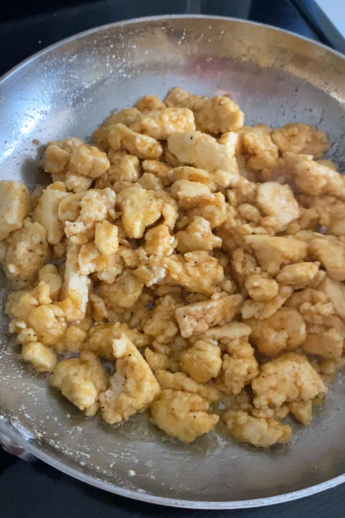 Crispy tofu fried in a stainless steel pan.