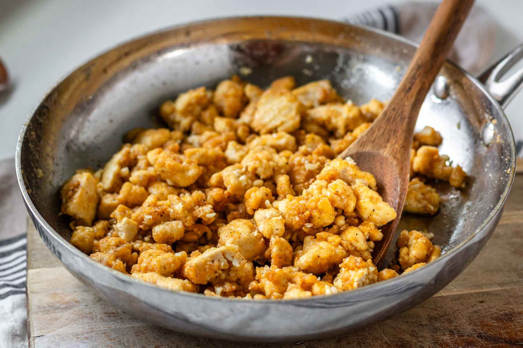 Garlic butter tofu in a stainless steel pan with a wooden spoon.