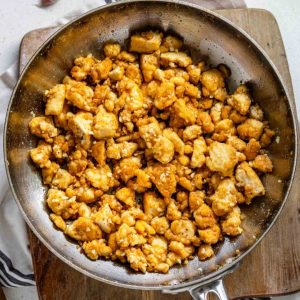 Garlic butter tofu in a stainless steel pan on top of a wooden board.