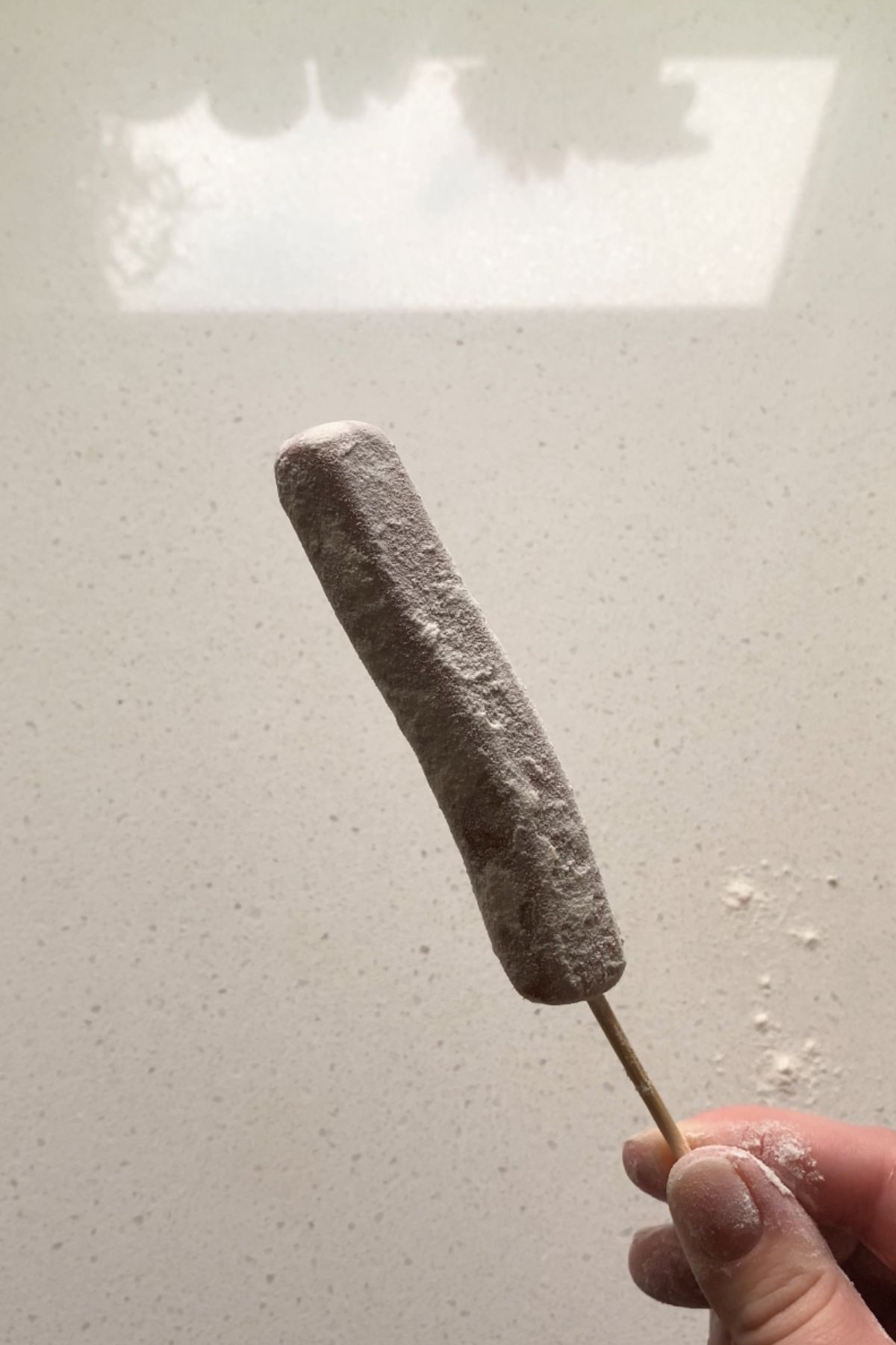 A skewered vegan corn dog coated in flour.