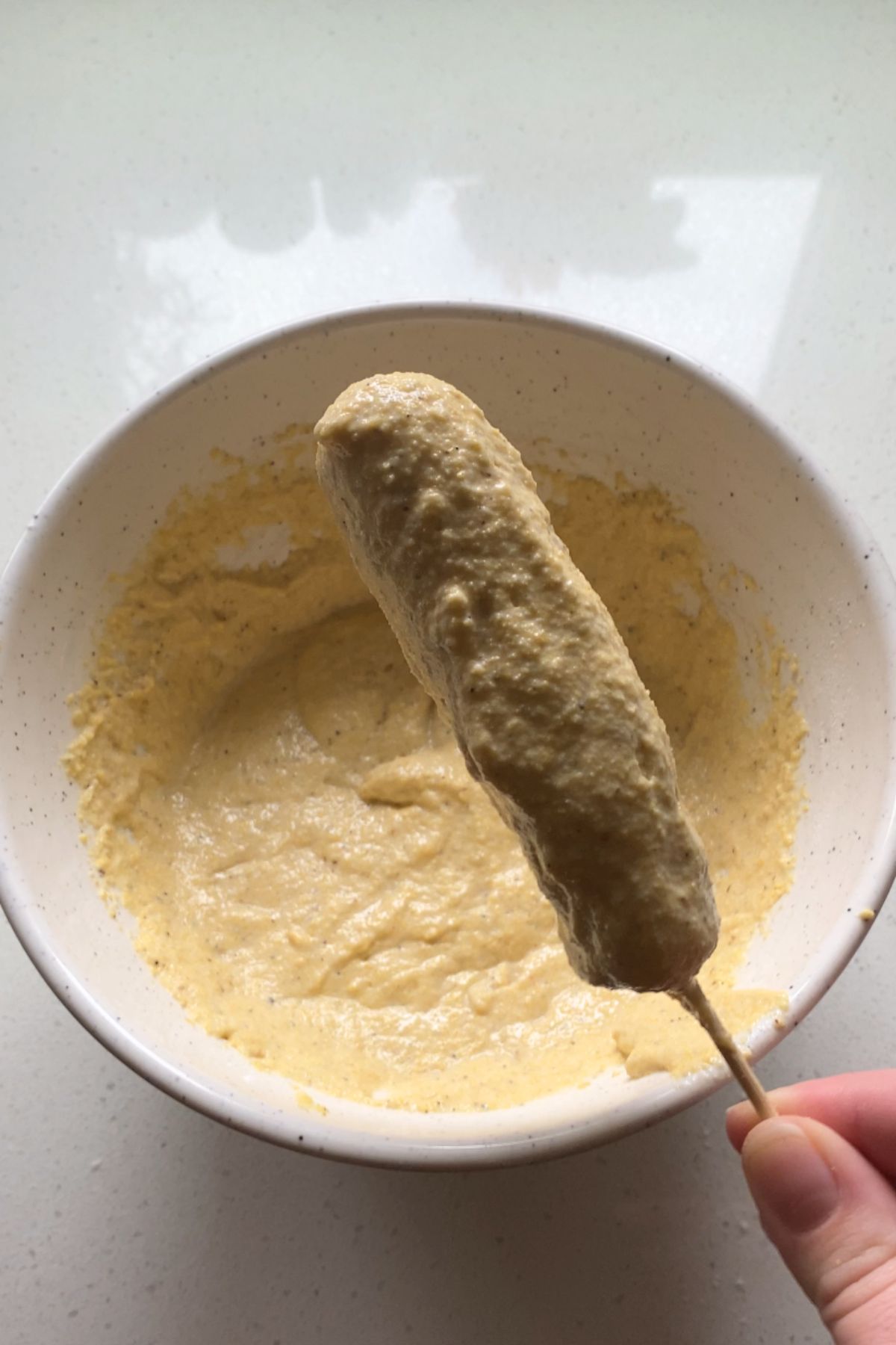 A skewered vegan hot dog coated in cornmeal batter.