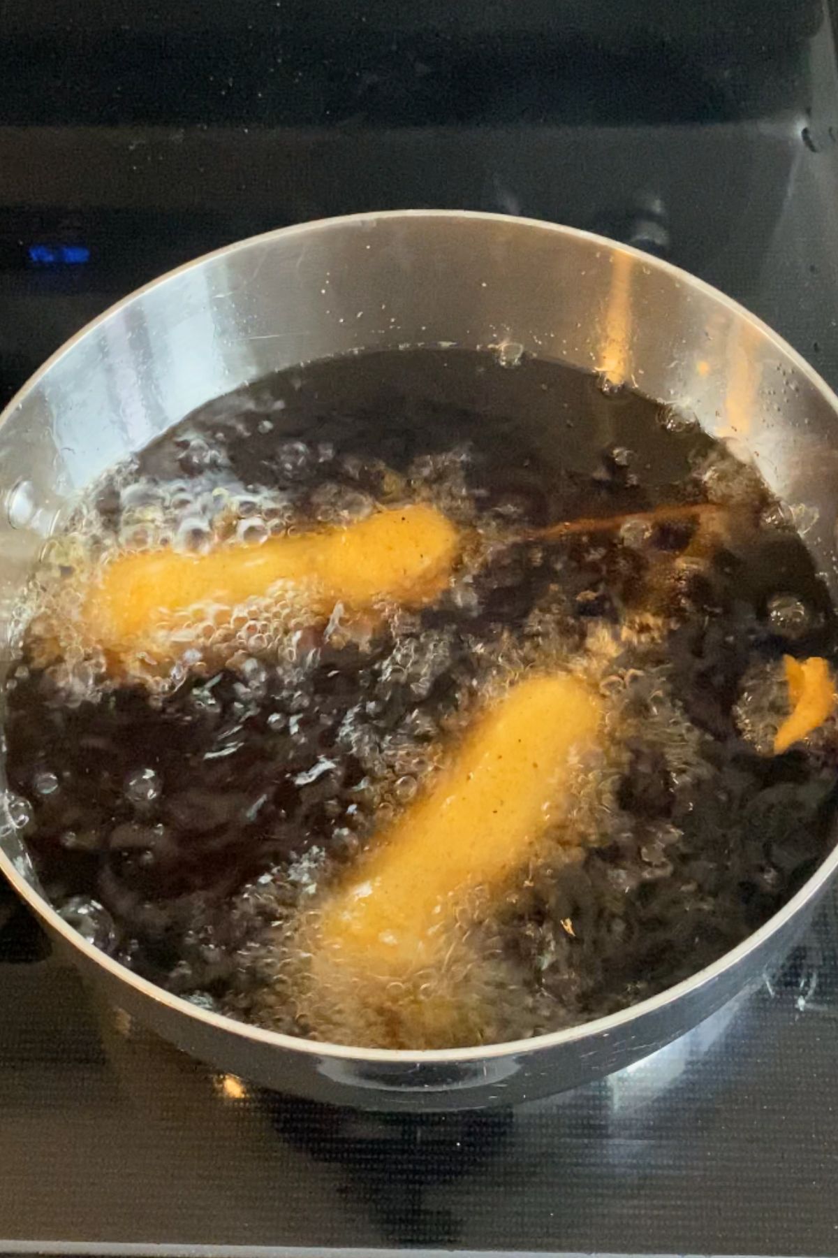 Two vegan corn dogs being deep fried in a large stainless steel pot.